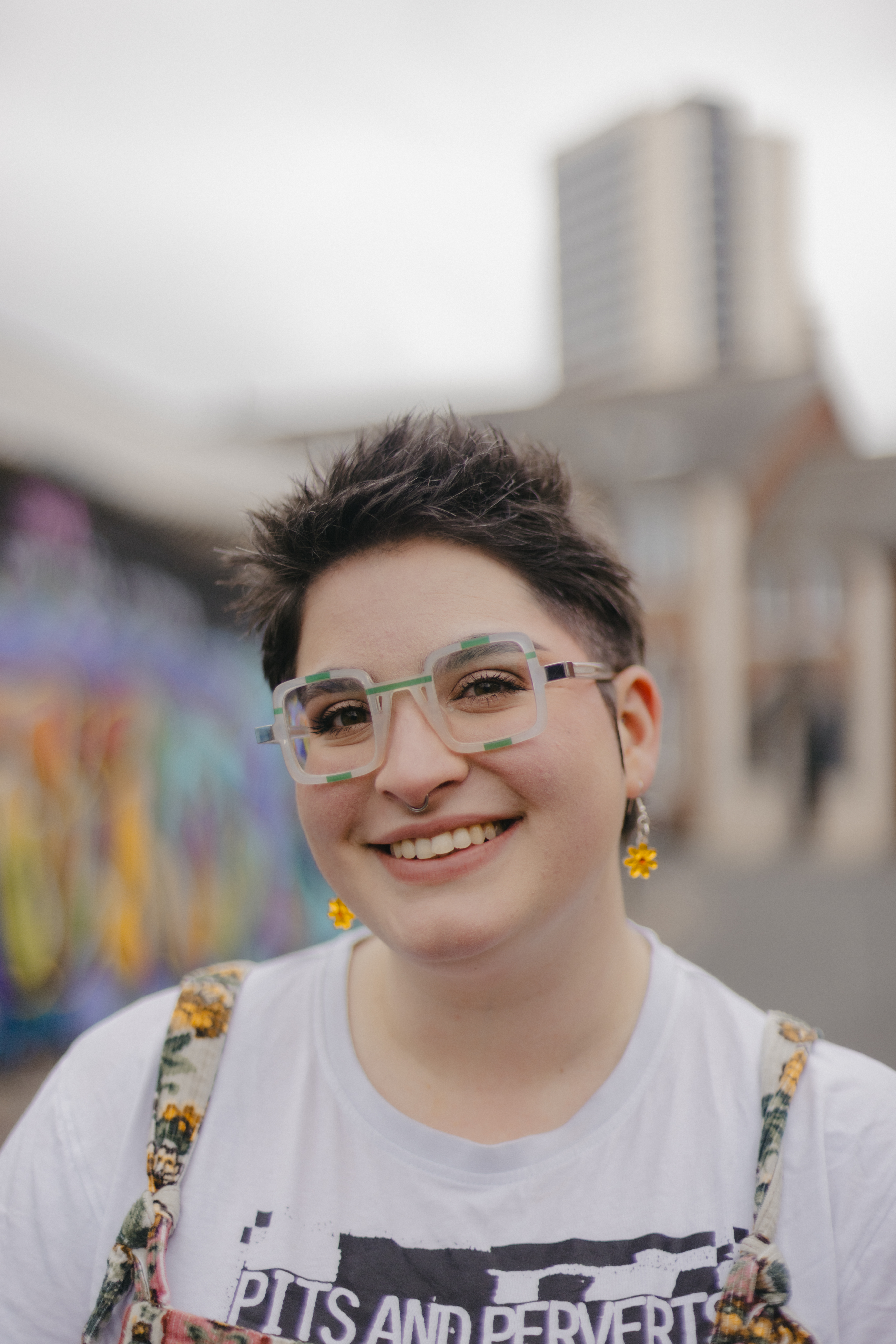 Amy Langdown Headshot Amy Langdown, brown spiky hair and square green glasses, giving a big cheesy grin