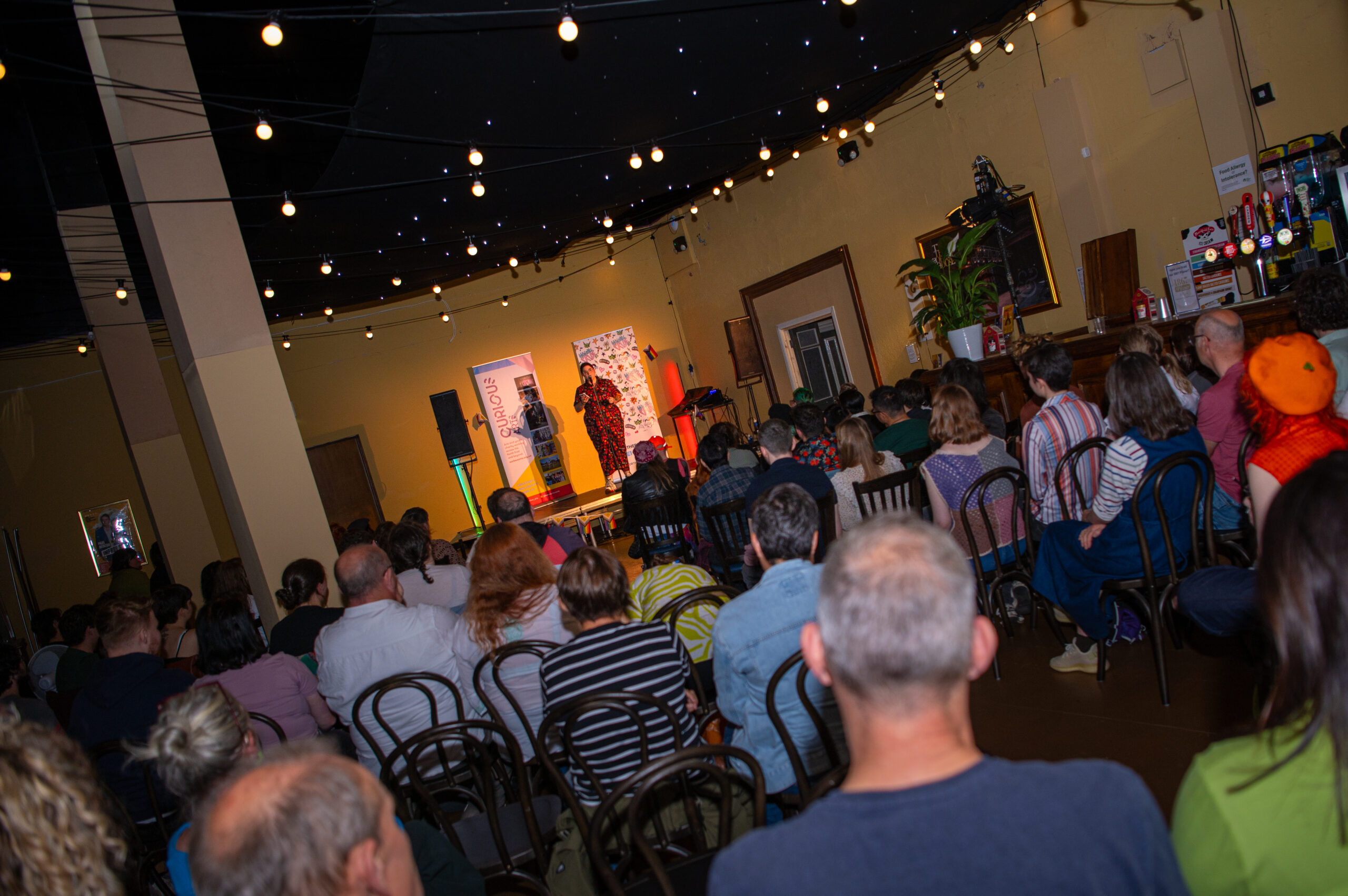 NCL pride OOYH a crowded room and in the distance you can see Amy on the stage at the Out of Your HEad Newcastle Pride 2025 event