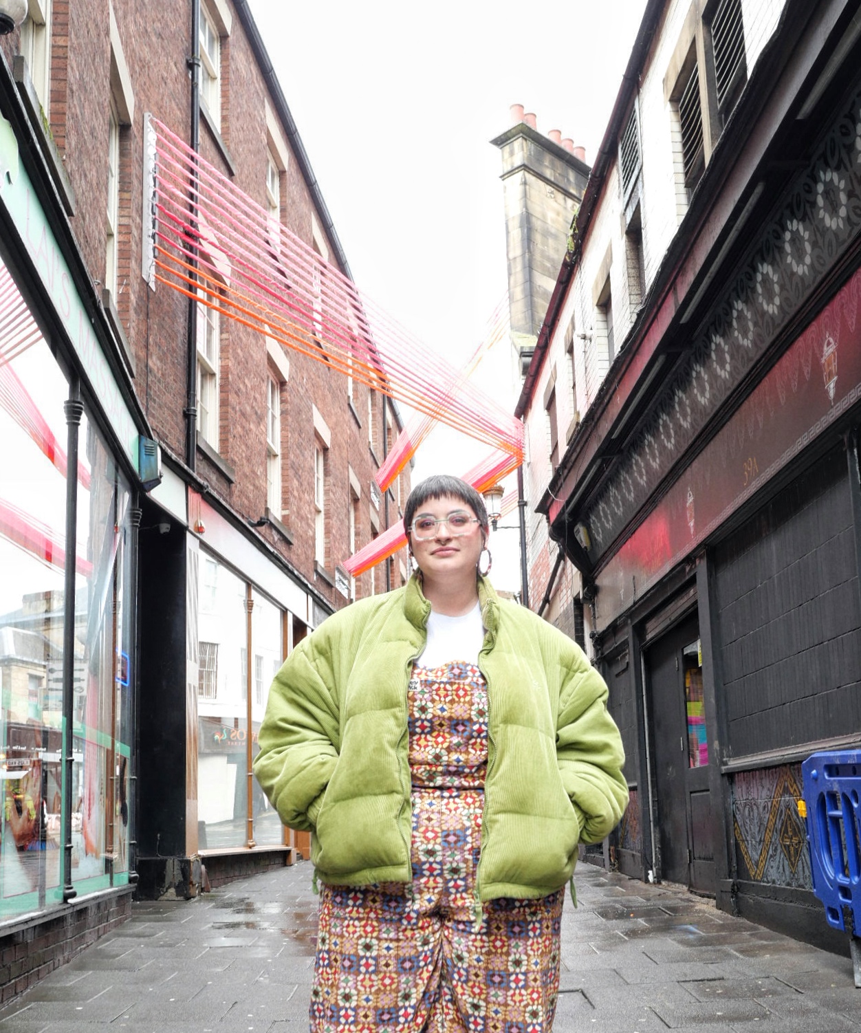Amy performing a poem, hand up in the air, in colourful arcade-carpet patterened dungarees